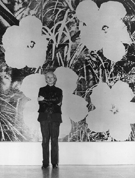 Andy Warhol standing in front of one of his large silk screen paintings of flowers, 15 January 1973. Image: Evening Standard/Getty Images.